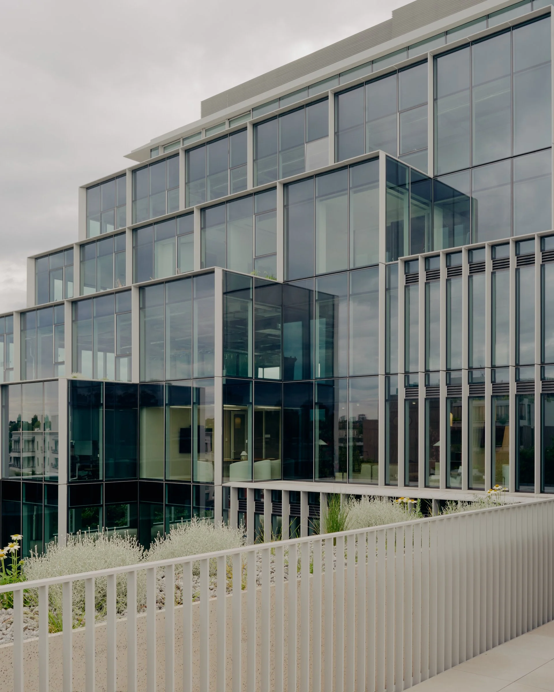 Modern multi-story glass office building with large windows and a white railing in the foreground.