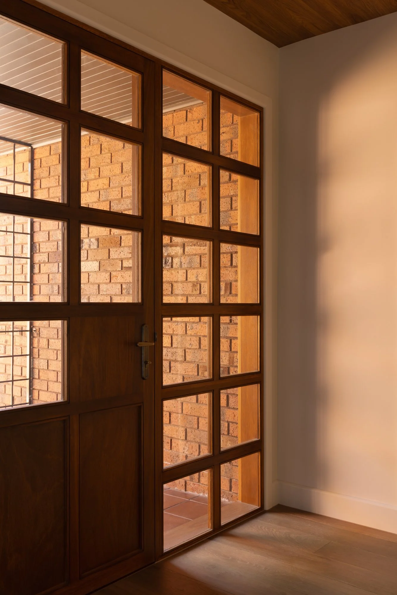 A sliding wooden door with glass panels opens to a brick patio or porch area outside, with sunlight illuminating the scene.