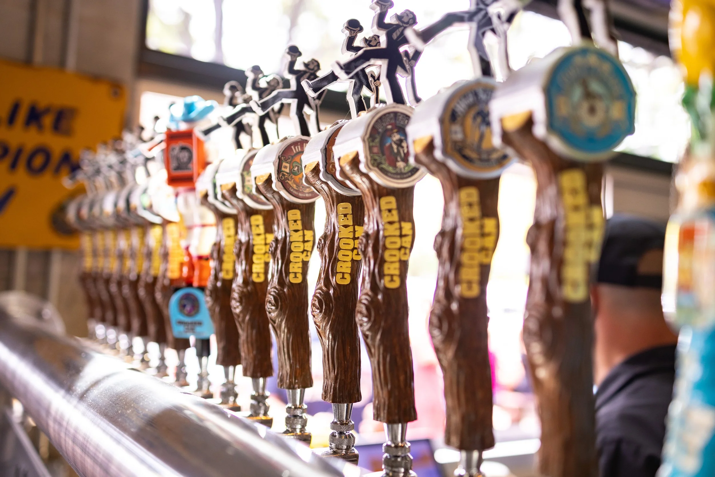 Multiple beer taps with CrossRoads Ale branding, arranged in a row at a bar, with a man partially visible in the background.