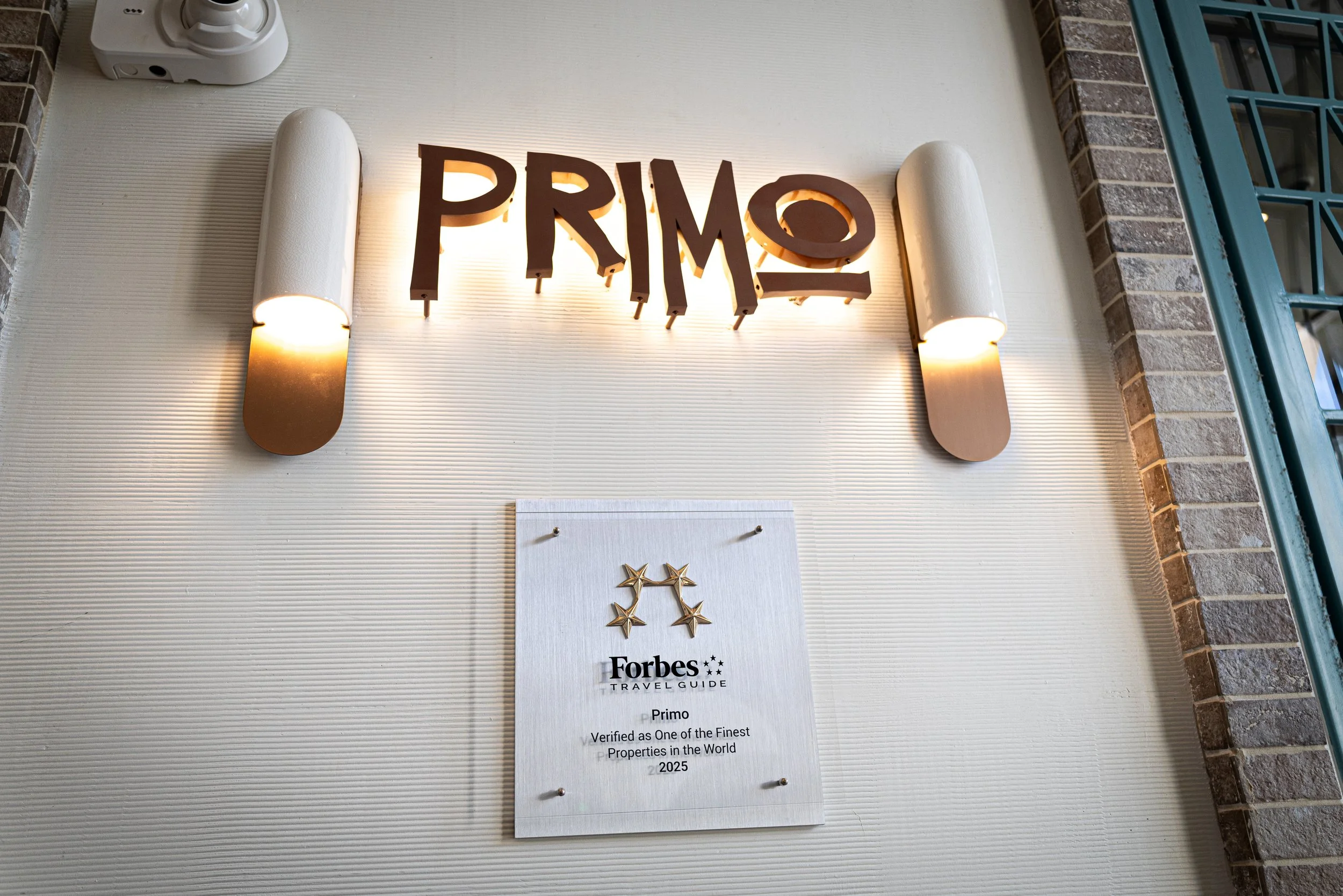 Sign with the word 'PRIMO' above a plaque awarded by Forbes Travel Guide, acknowledging it as one of the finest properties in the world in 2025.
