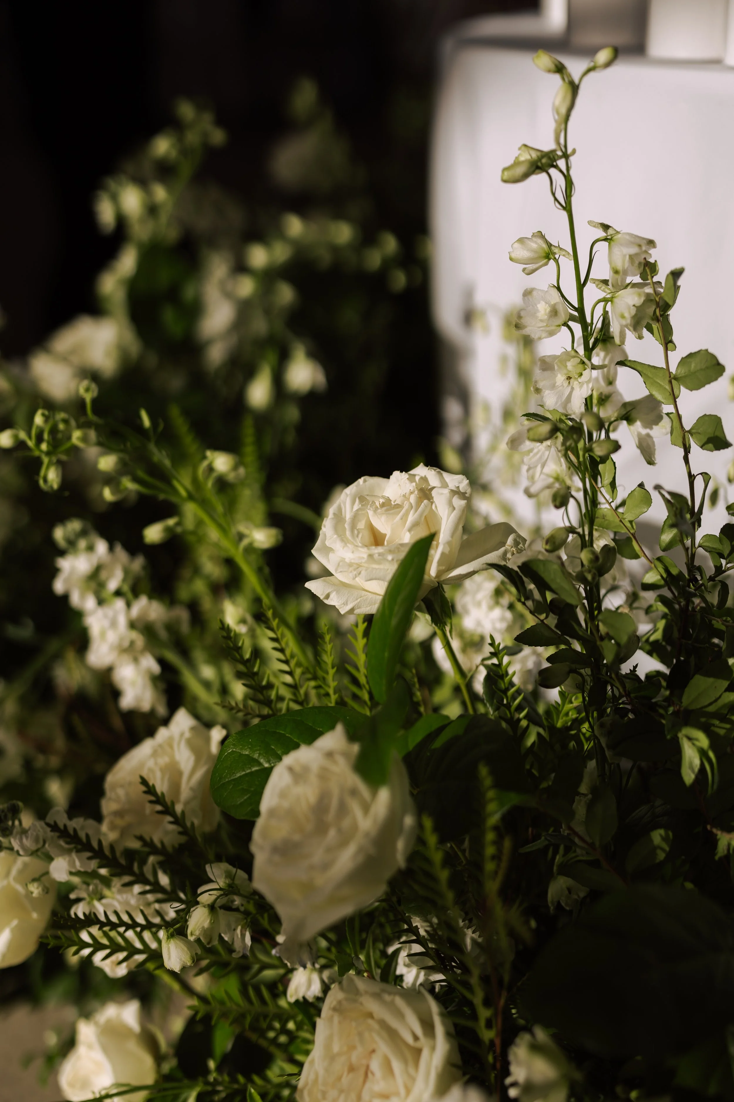 A close-up of a floral arrangement with white roses and various white flowers and green leaves.