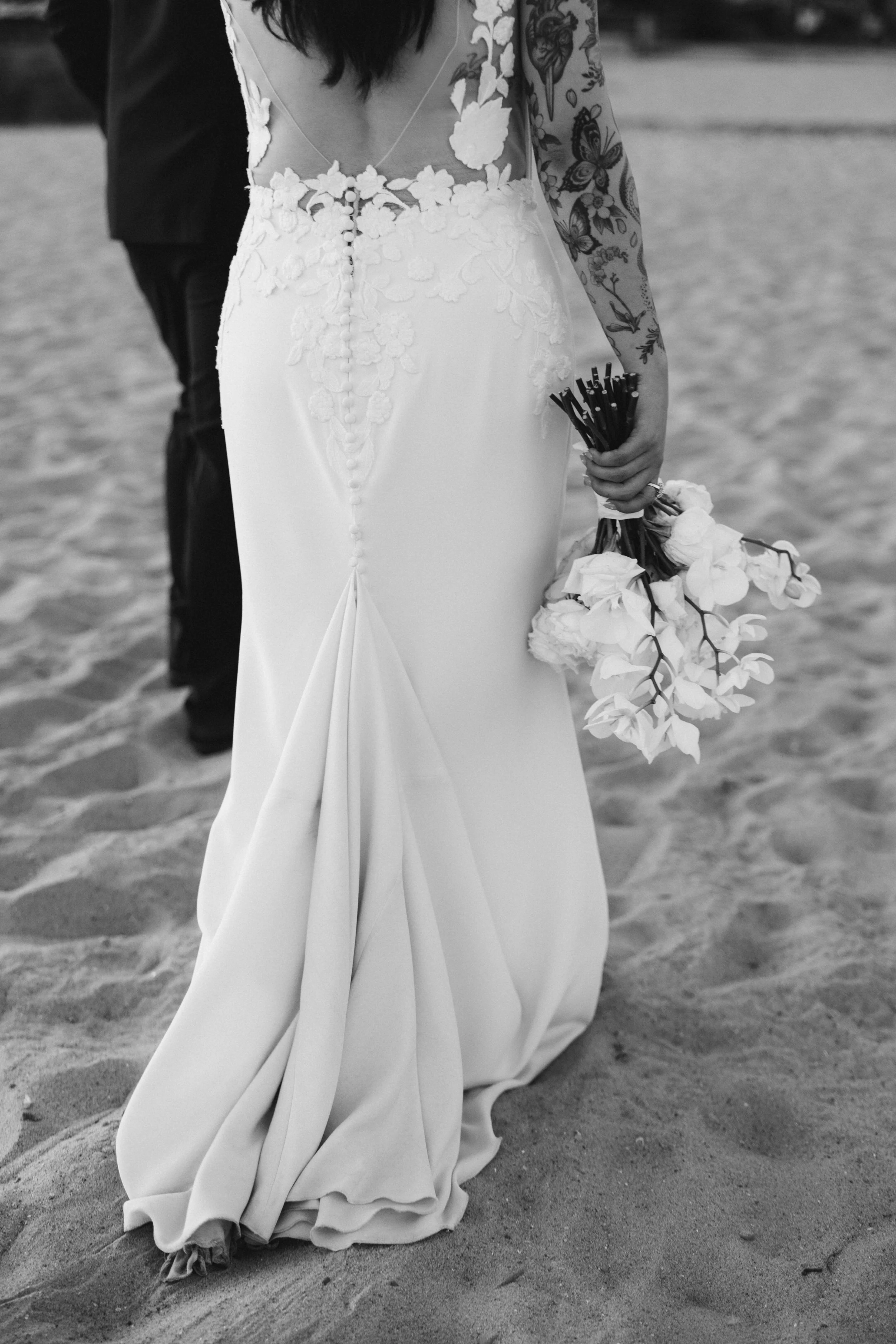 A woman in a wedding dress holding a bouquet of flowers on a sandy beach.