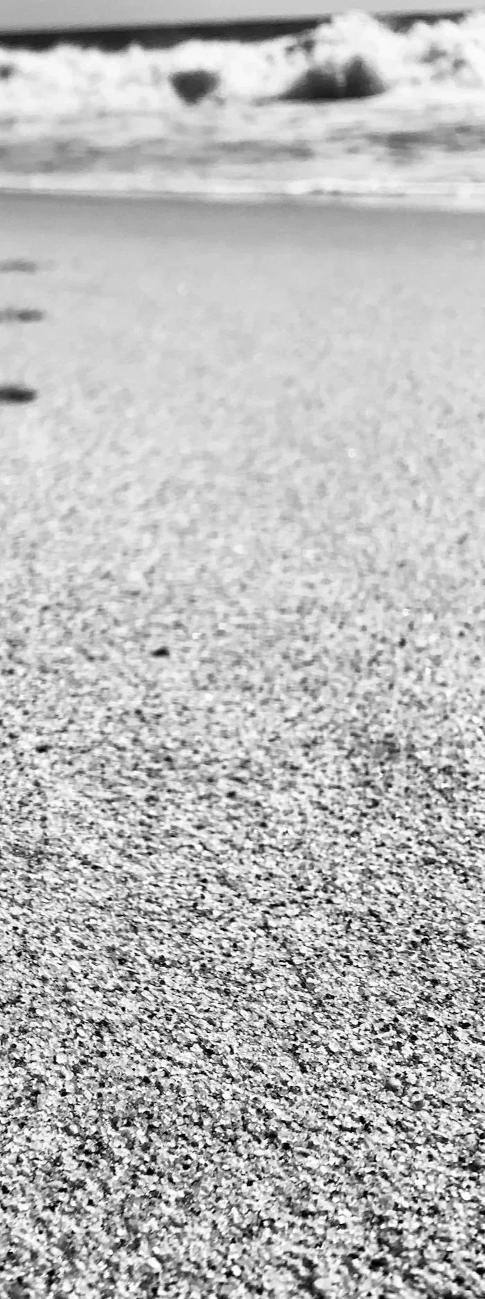 Close-up of sandy beach with ocean waves in the background, black and white image.