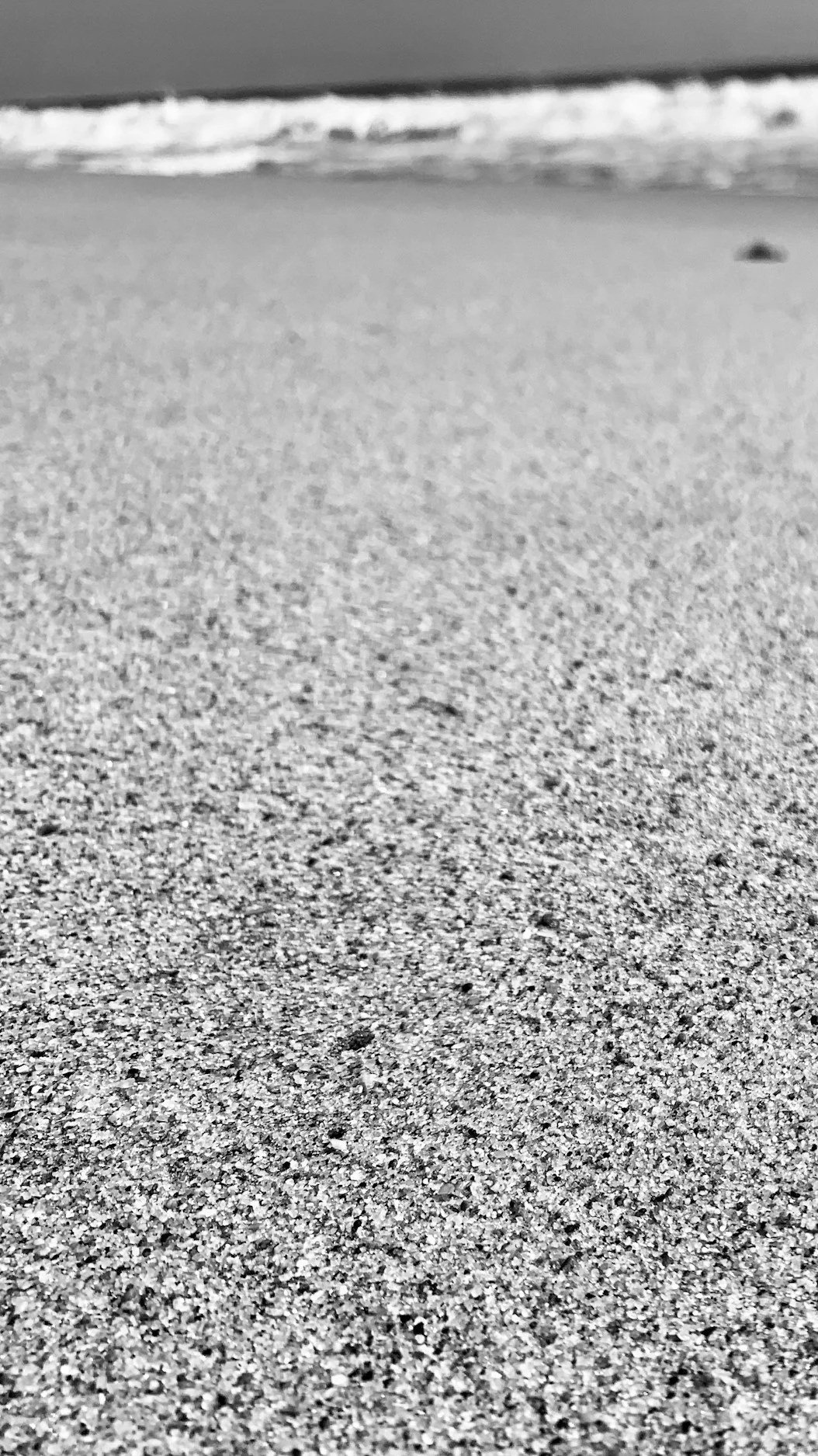 Black and white photo of a sandy beach with waves in the background.