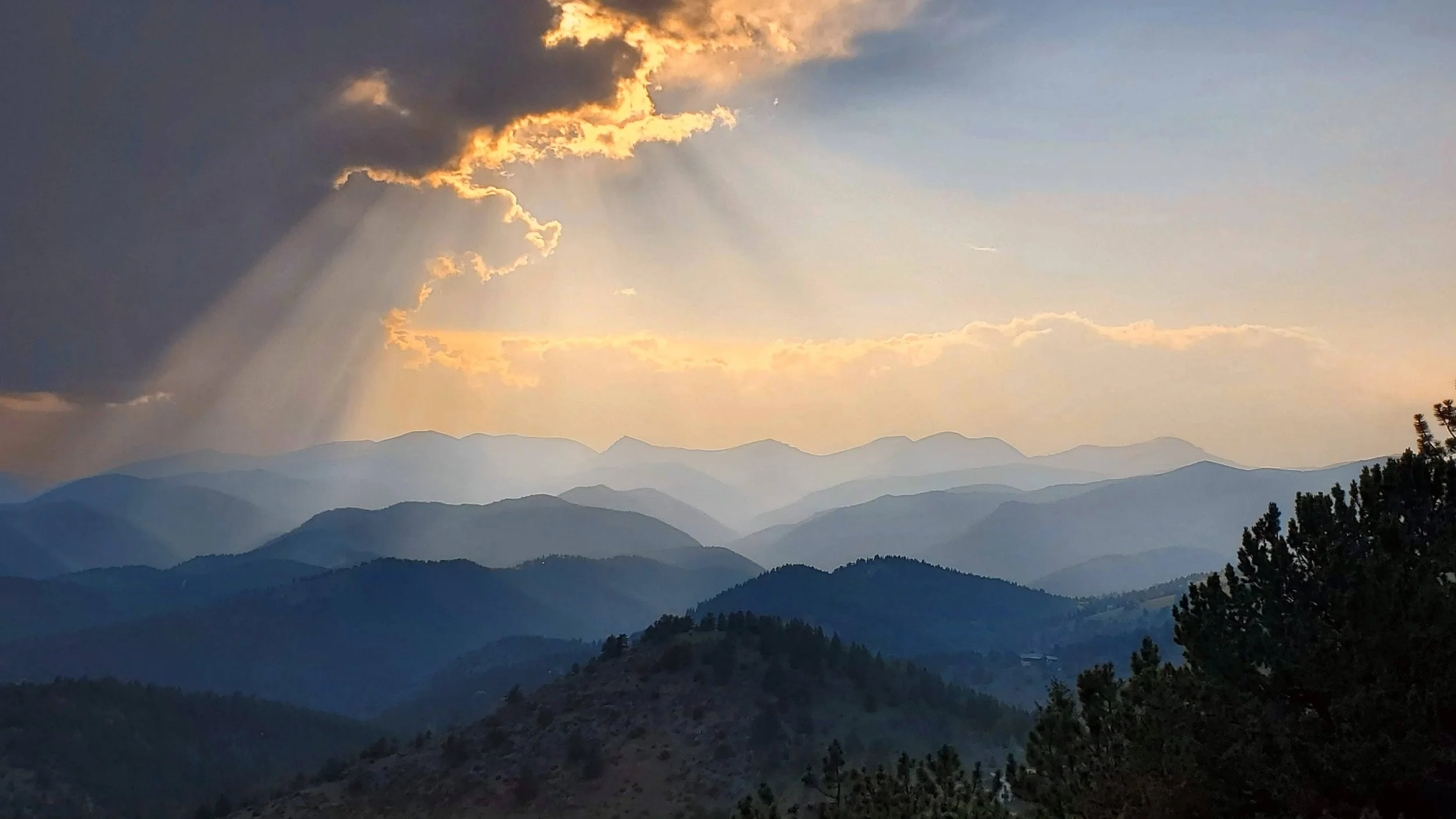 Mountain landscape with multiple ridges in the distance under a sky with clouds and sunlight rays.