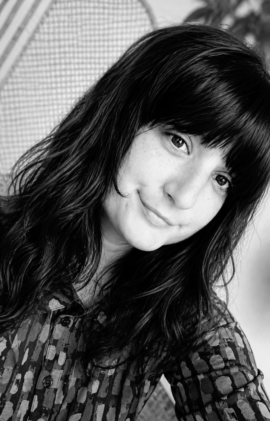 Porträt einer jungen Frau mit dunklen, gewellten Haaren und heller Haut, die ein gemustertes Hemd trägt, in Schwarz-Weiß