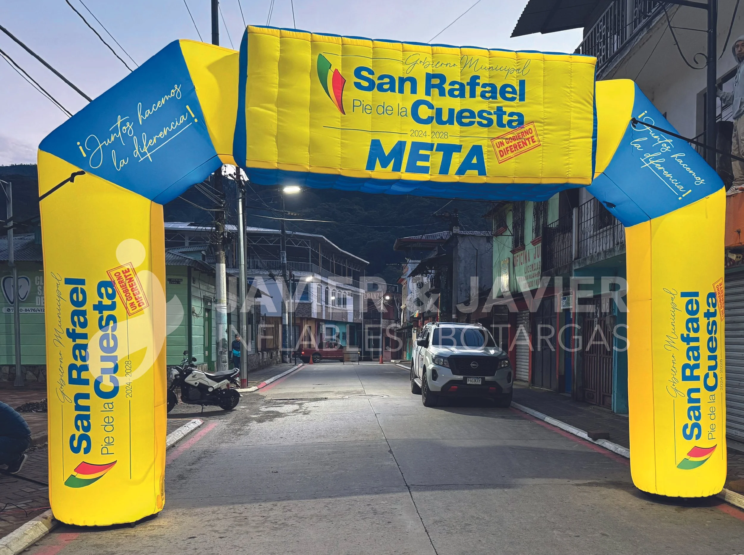 Un arco inflable con colores azul y amarillo en una calle, con texto en español que dice 'San Rafael Pie de la Cuesta META', y frases de campaña política '¡Juntos hacemos la diferencia!' y 'Un gobierno diferente'.