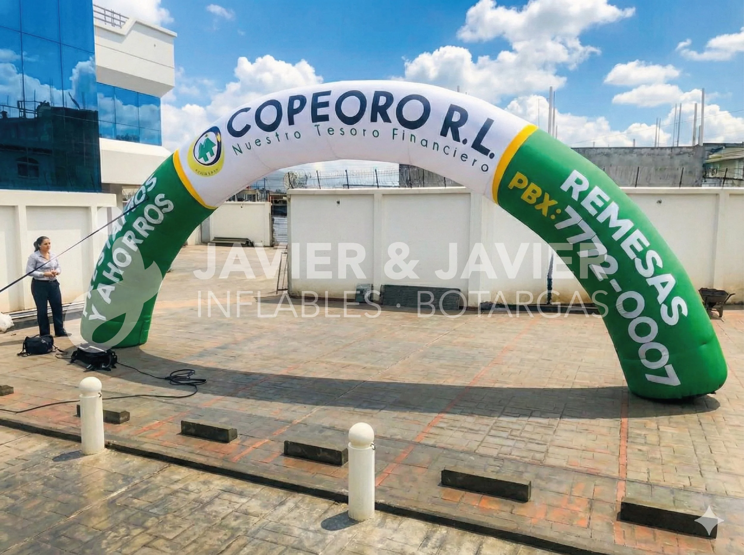 Arco inflable grande en color verde y blanco con texto promocional, instalado en un espacio abierto con un edificio de vidrio en el fondo y cielo soleado con nubes blancas.