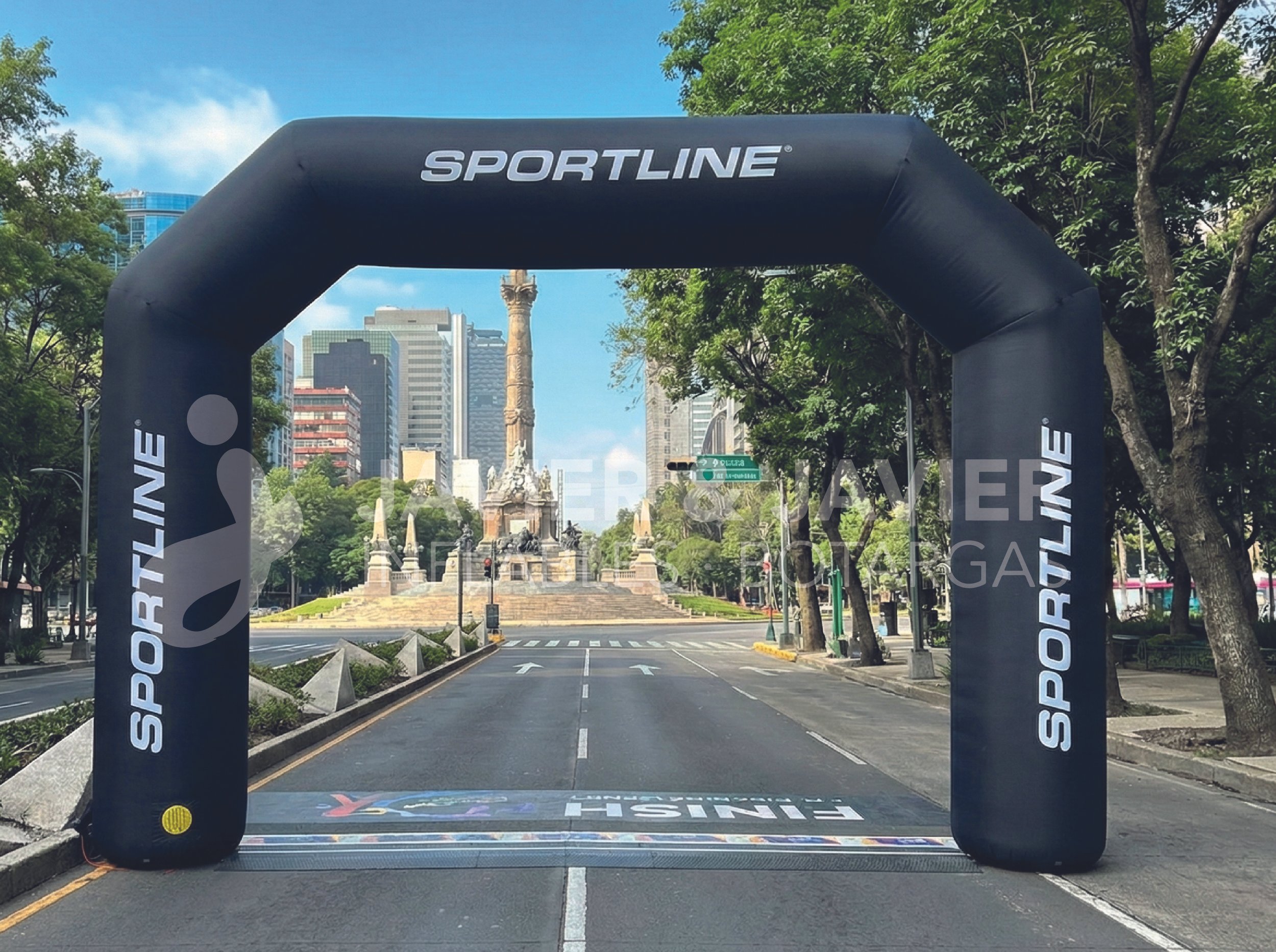 Arco inflable de color negro con la palabra 'SPORTLINE' en la parte superior, altura en medio y en los lados, colocado en una calle de ciudad con árboles, edificios y una plaza con monumento en el fondo.
