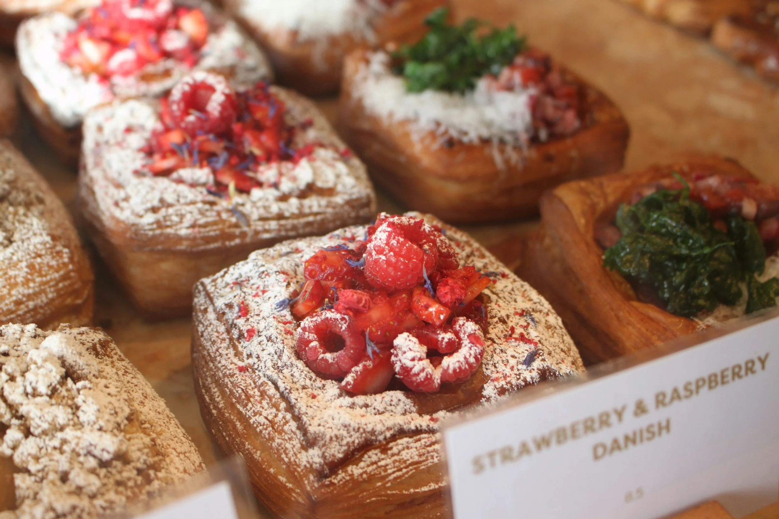 Assorted Danish pastries topped with berries, powdered sugar, and decorative edible flowers on a display tray.