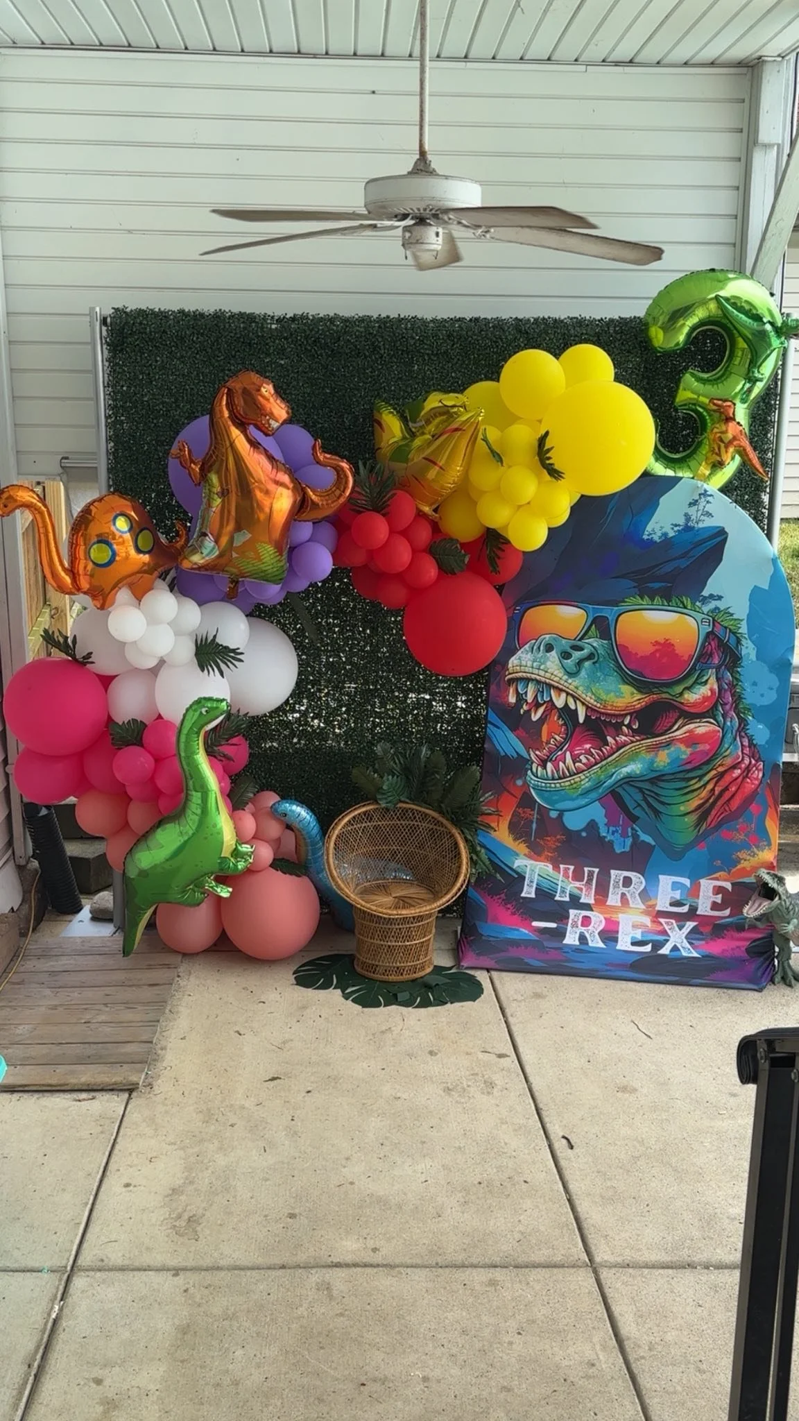 Three-rex birthday party balloon decor peacock chair and greenery wall. Dayton ohio