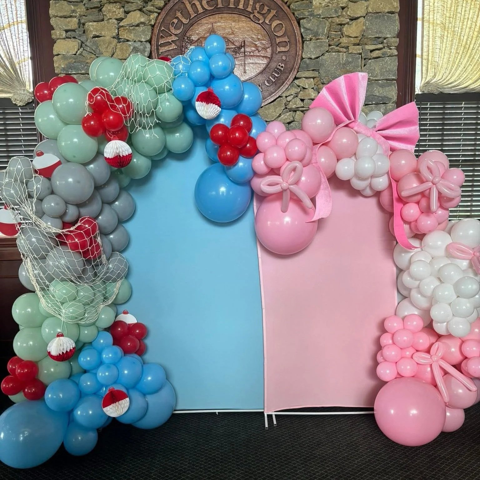 Creative bows and bobbers balloon backdrop with pastel pink and blue balloon garlands, fishing net details, balloon bows, and balloon bobbers, designed for a baby shower or gender reveal celebration.