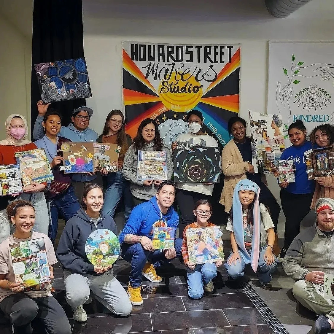 Group of adults and children holding artwork and paintings at an art studio event.