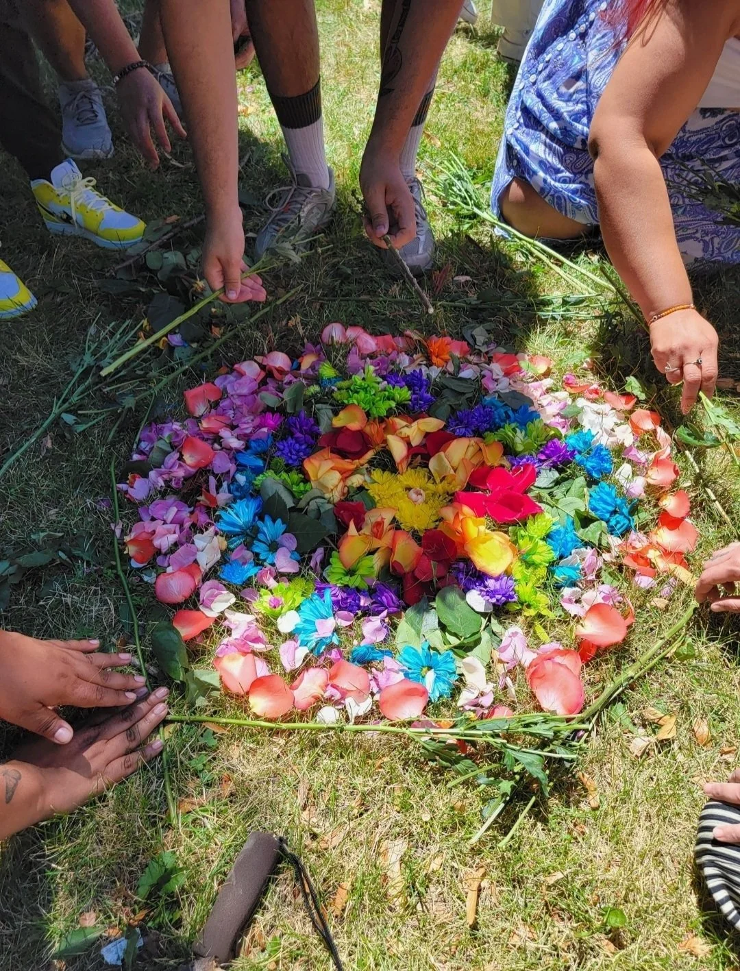 People placing colorful flowers on the ground in a circular arrangement.