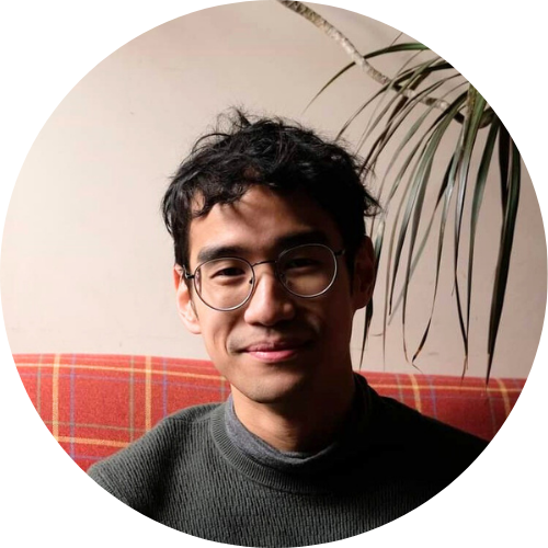 Portrait of David Tran smiling at the camera, wearing a grey shirt and glasses.