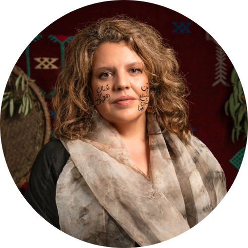 A woman with Arabic calligraphy adorning her face. The background features traditional Palestinian tatreez embroidery patterns along with decorative ornamental elements.