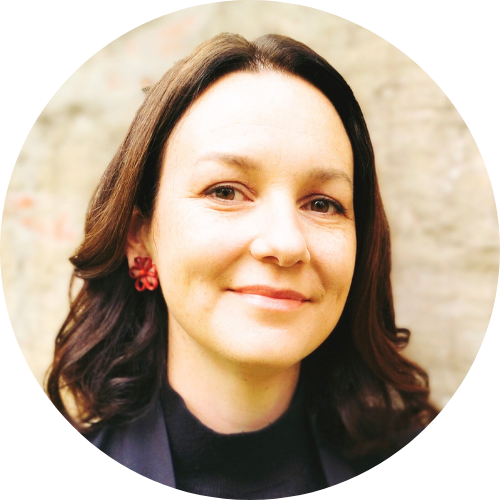 Ika Trijsburg wearing a navy jacket, black shirt and red flower earrings.