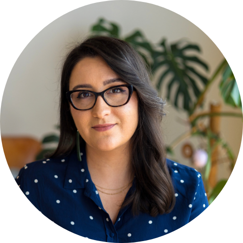 Kera Sherwood-O'Regan, a Māori woman with brown and grey hair, wearing tortoiseshell glasses, and wearing pounamu greenstone earrings. She is wearing a navy and white dotted silk shirt.