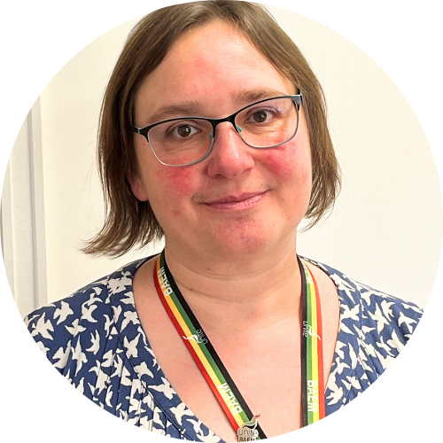 Portrait of Heather Blakey smiling at the camera, wearing a patterned shirt, rainbow lanyard and glasses.