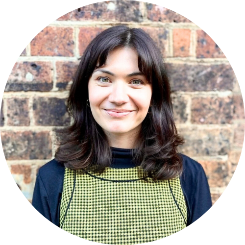 Portrait of Maddie Burkitt standing in front of a brick wall, smiling facing the camera.