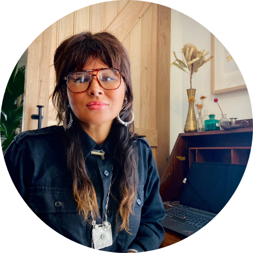 A long-haired woman with glasses sits next to her laptop.