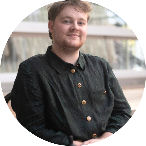 An androgynous white young person sitting in a wheelchair and smiling at the camera.