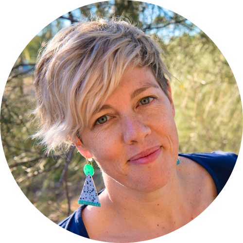Alex Kelly smiling, facing the camera, wearing triangle earrings and a blue shirt.