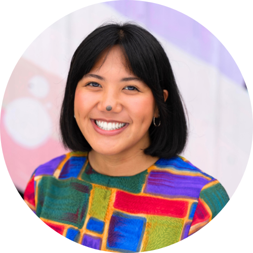 Selah [Filipina, short black hair] is smiling wearing a colorful blouse.