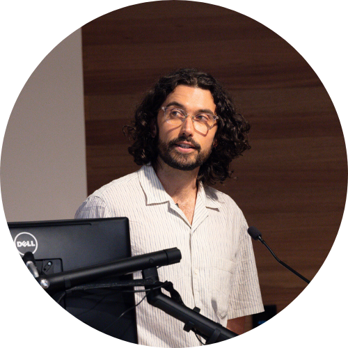 Alistair stands at lecturn, with screen in corner adressing audience.