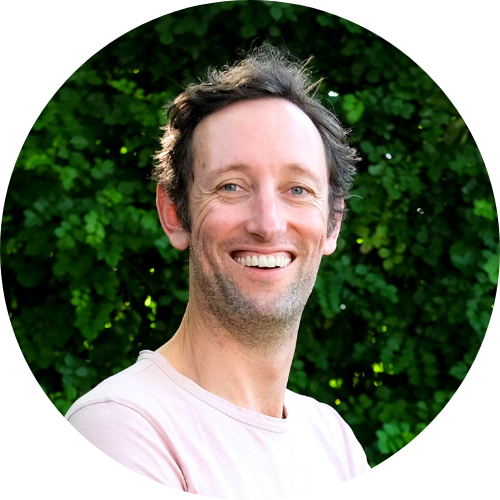 A photo of Andrew Hudson, who is smiling against a backdrop of green trees.