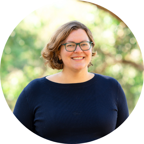 A photo of a white woman wearing glasses standing outside near trees