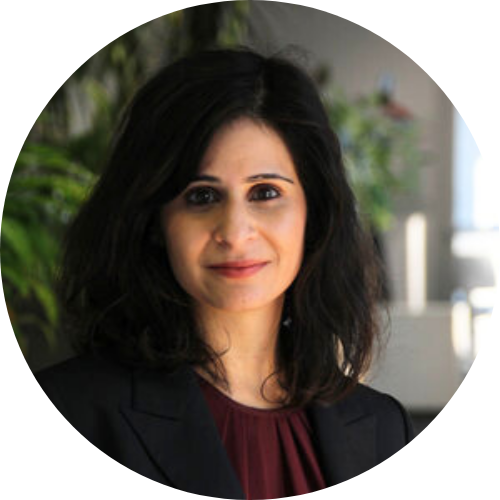 A woman with dark mid-length hair and olive complexion wearing a suit jacket and dark red blouse