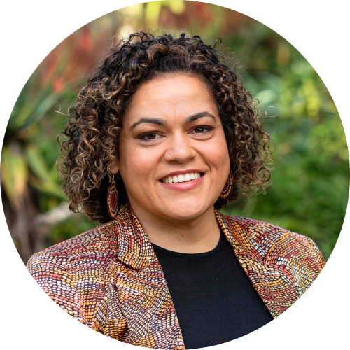Portrait of Larissa Baldwin-Roberts outdoors, smiling facing the camera  with a black shirt and patterned jacket.