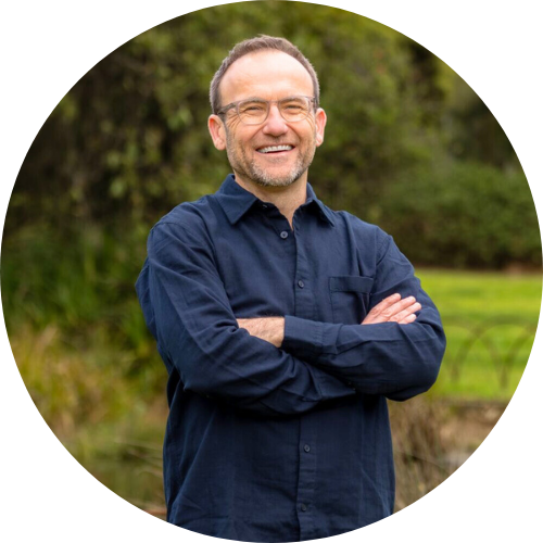 Adam Bandt stands outdoors with arms crossed, smiling.
