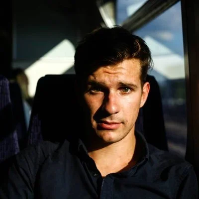 Joe Todd facing camera, seated on bus with sun angled in.