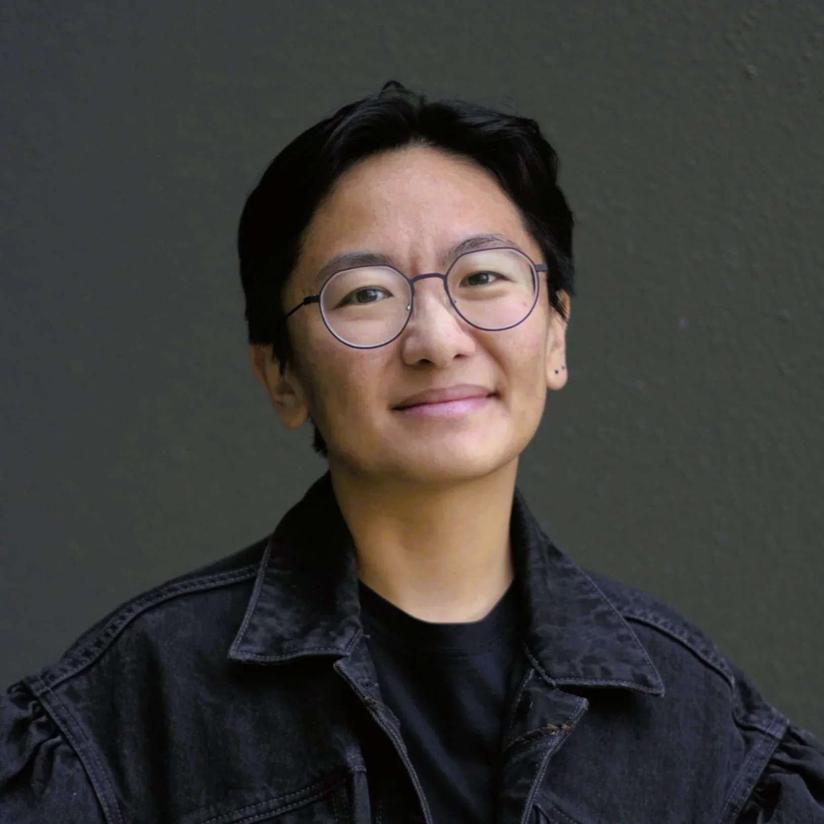 Jinghua Qian smiling, facing the camera, wearing glasses and a black jacket.