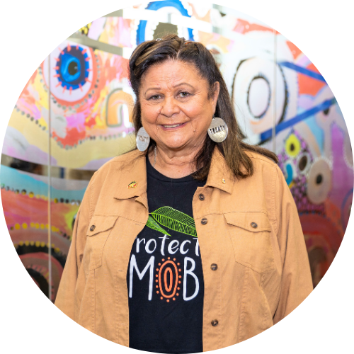 Dr Jill Gallagher AO, wearing a Protect Mob shirt against a colourful backdrop