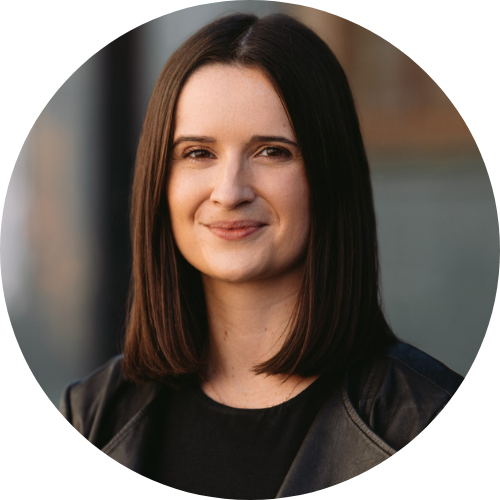 A woman with dark brown chin-length hair, wearing a black top and jacket, looks at the camera with a calm, slight smile against a softly blurred background.