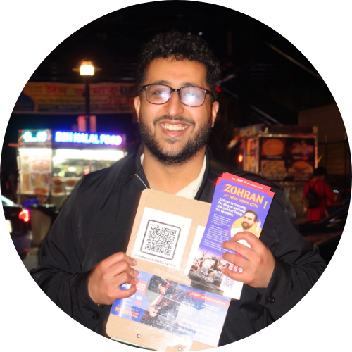 Image of Mohamed smiling at the camera holding Zohran for NYC flyers and a clipboard with a volunteering QR code.