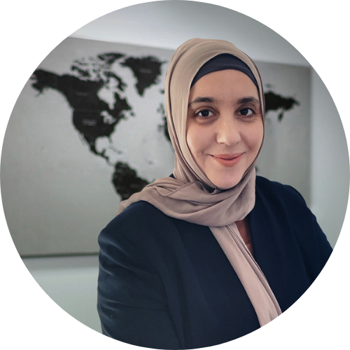 A portrait of Rita Jabri Markwell smiling, wearing a hijab and a suit