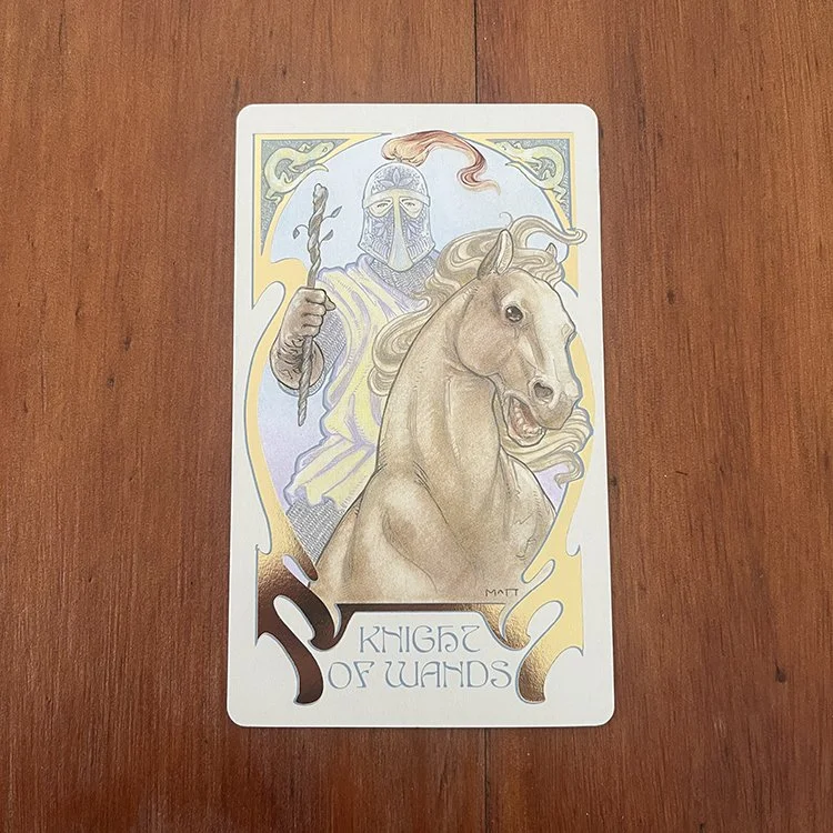 The Sun of Wands tarot card showing a knight on a horse holding a staff with a flag on top, depicted in pastel and gold tones.