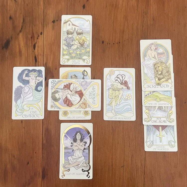 A spread of tarot cards laid out on a wooden surface, including The World, The Star, The Chariot, The Lovers, Two of Pentacles, Six of Wands, and Eight of Swords.