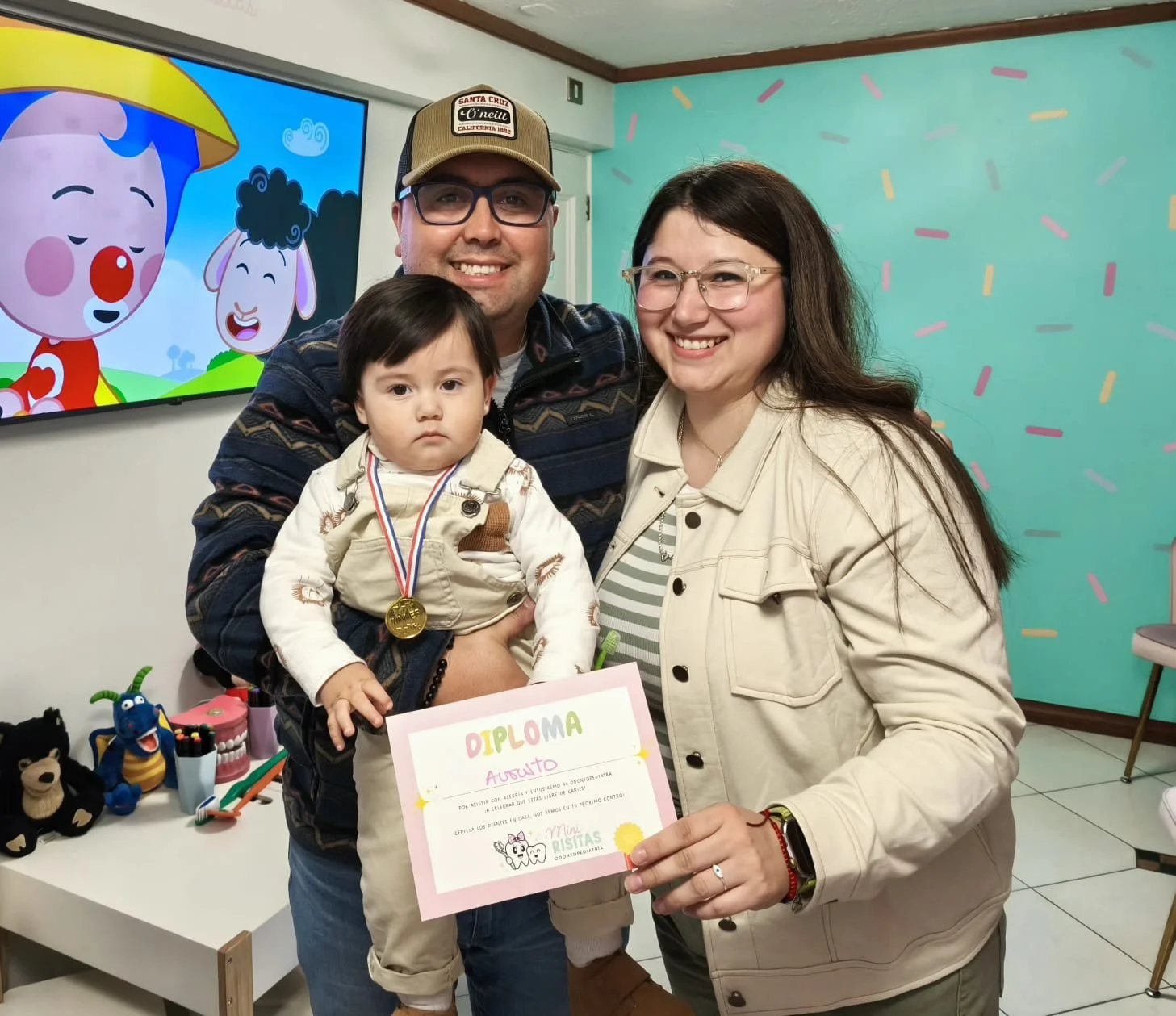 Familia feliz en celebración infantil, con un niño con medalla y diploma, acompañados por dos adultos sonriendo.