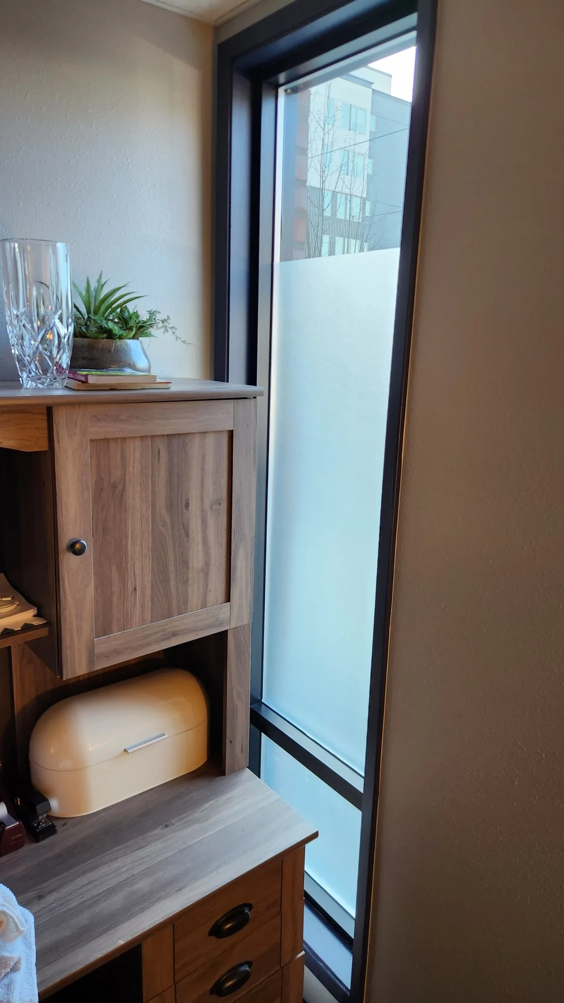 Close-up of a wooden cabinet next to a frosted glass window with modern buildings outside.