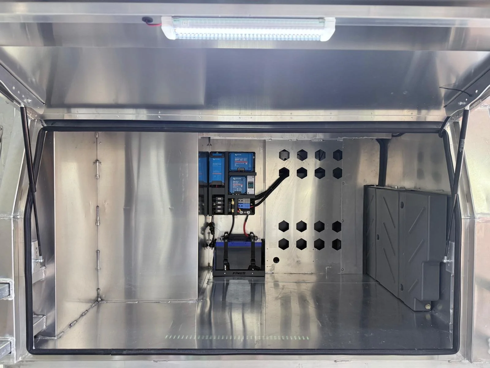 Inside an empty metallic enclosure or panel with electronic components and wiring, including a battery pack on the right side.