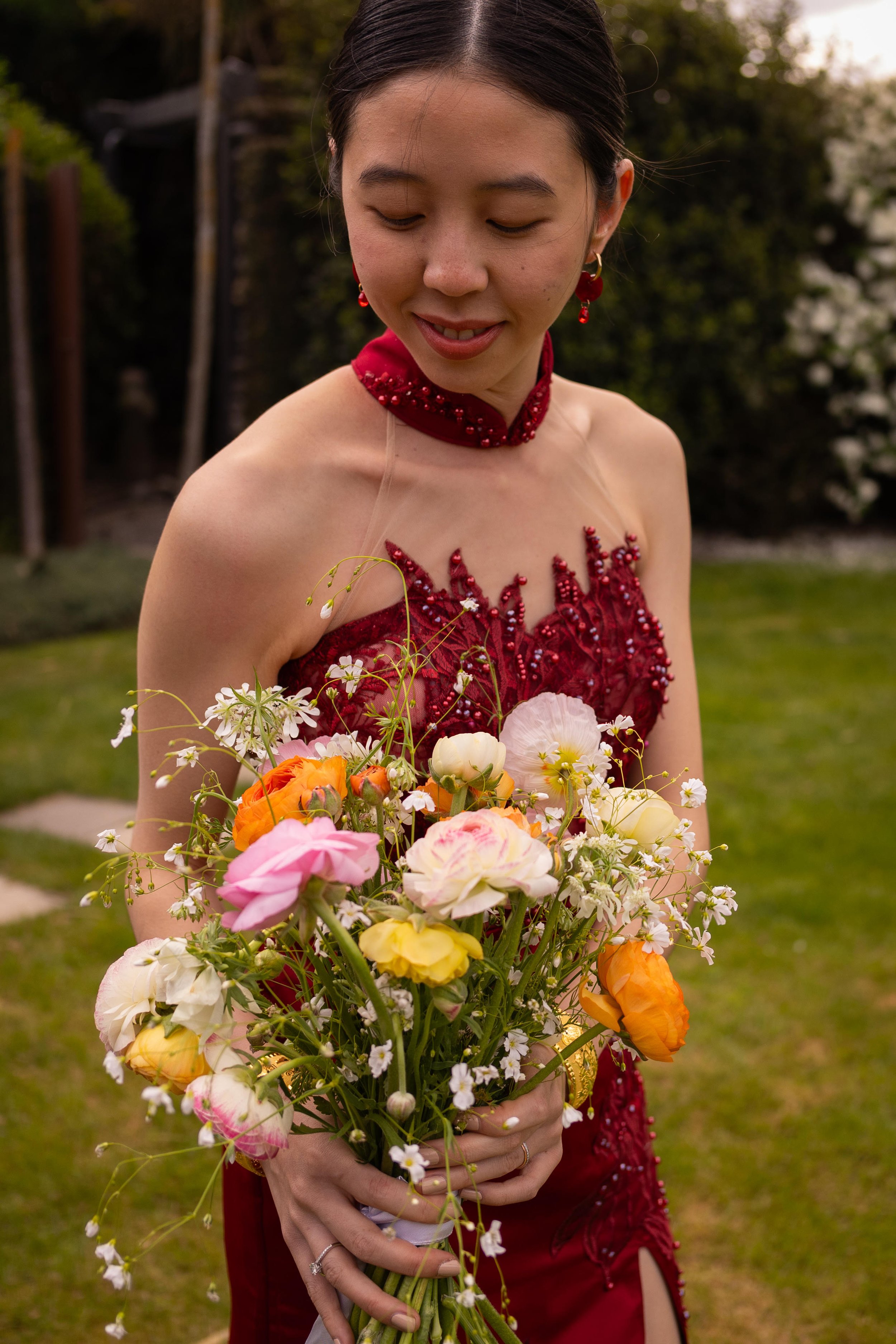 A woman in a red dress holding a colorful bouquet of flowers outdoors.