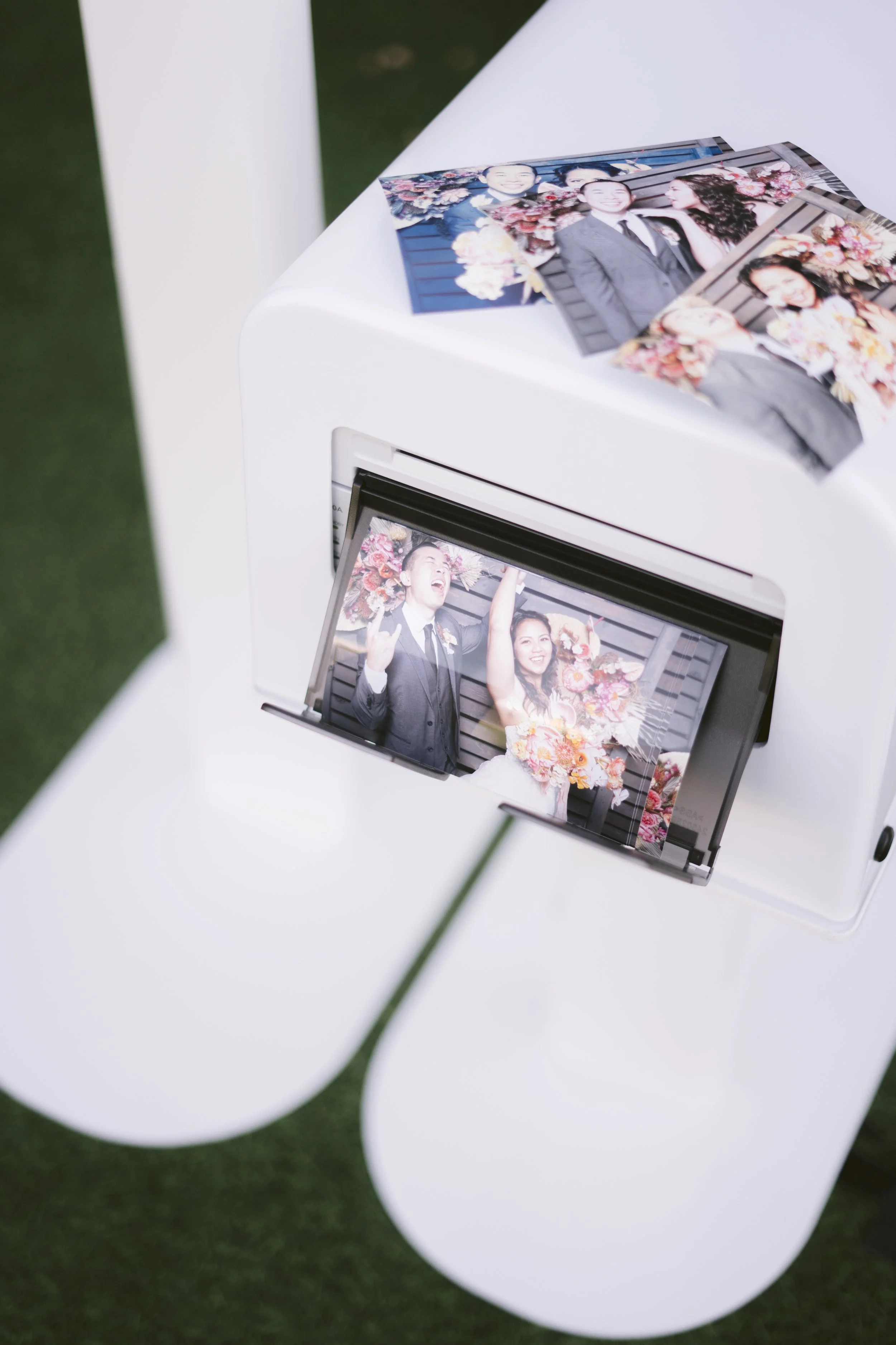 Photo booth printer producing event photo prints as they come out of the machine during a live photo booth experience. Keywords: photo booth prints, event photo booth rental, wedding entertainment, digital sharing, West Tennessee vendors.