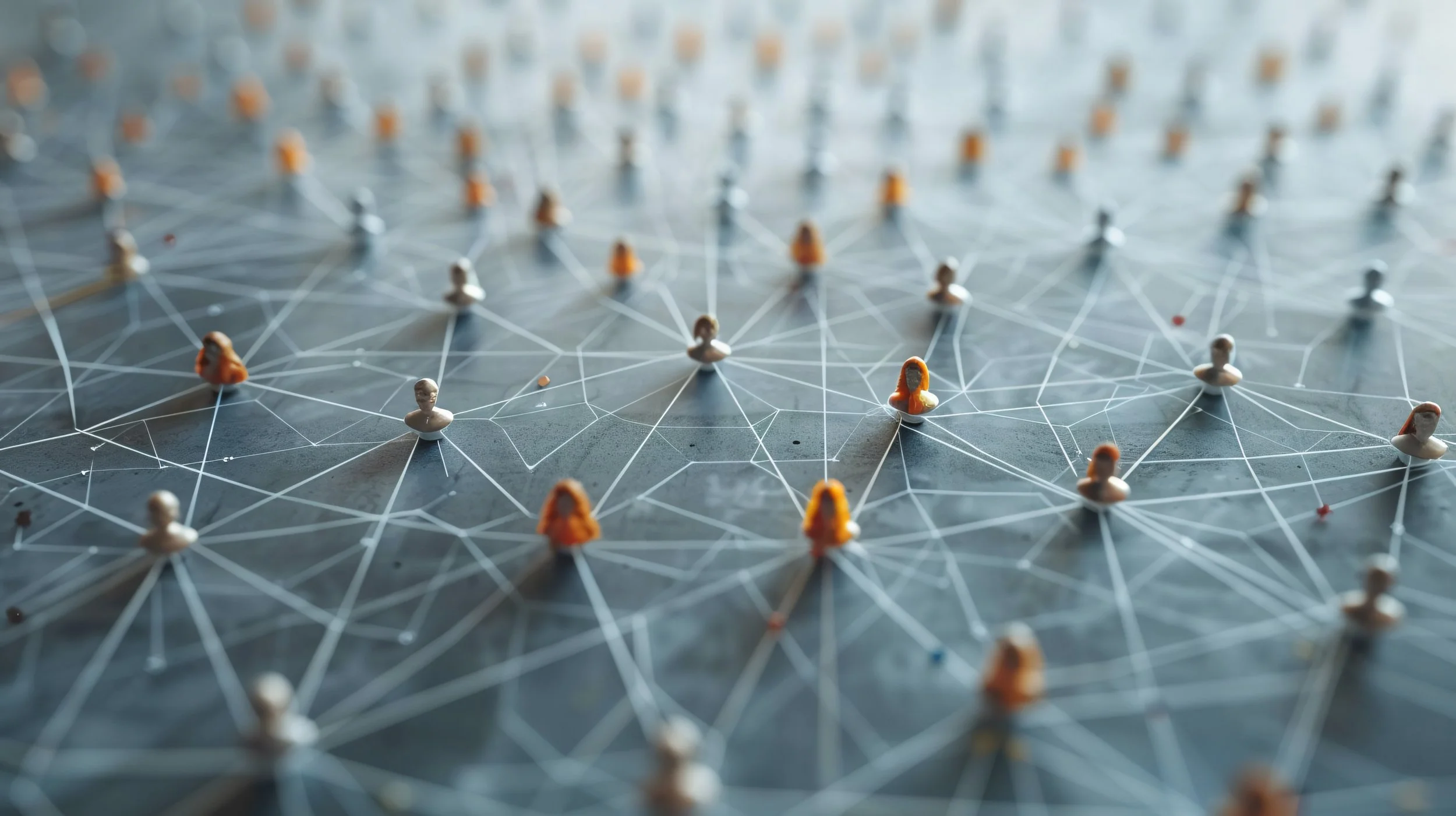 A network of interconnected white lines on a dark surface, with small humanoid figure figurines placed at intersections, representing a social or technological network.