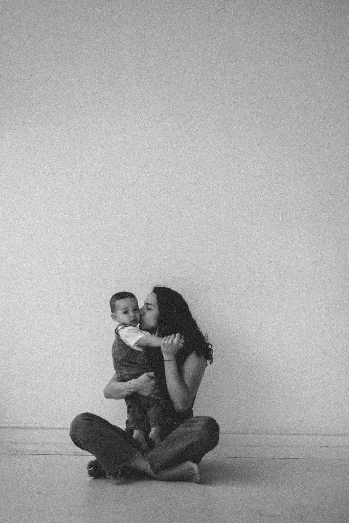 Black and white portrait of mother holding and kissing her baby in a minimal studio setting, captured by a Seattle lifestyle photographer. Emotional, timeless image focused on connection, motherhood, and intimate family moments.