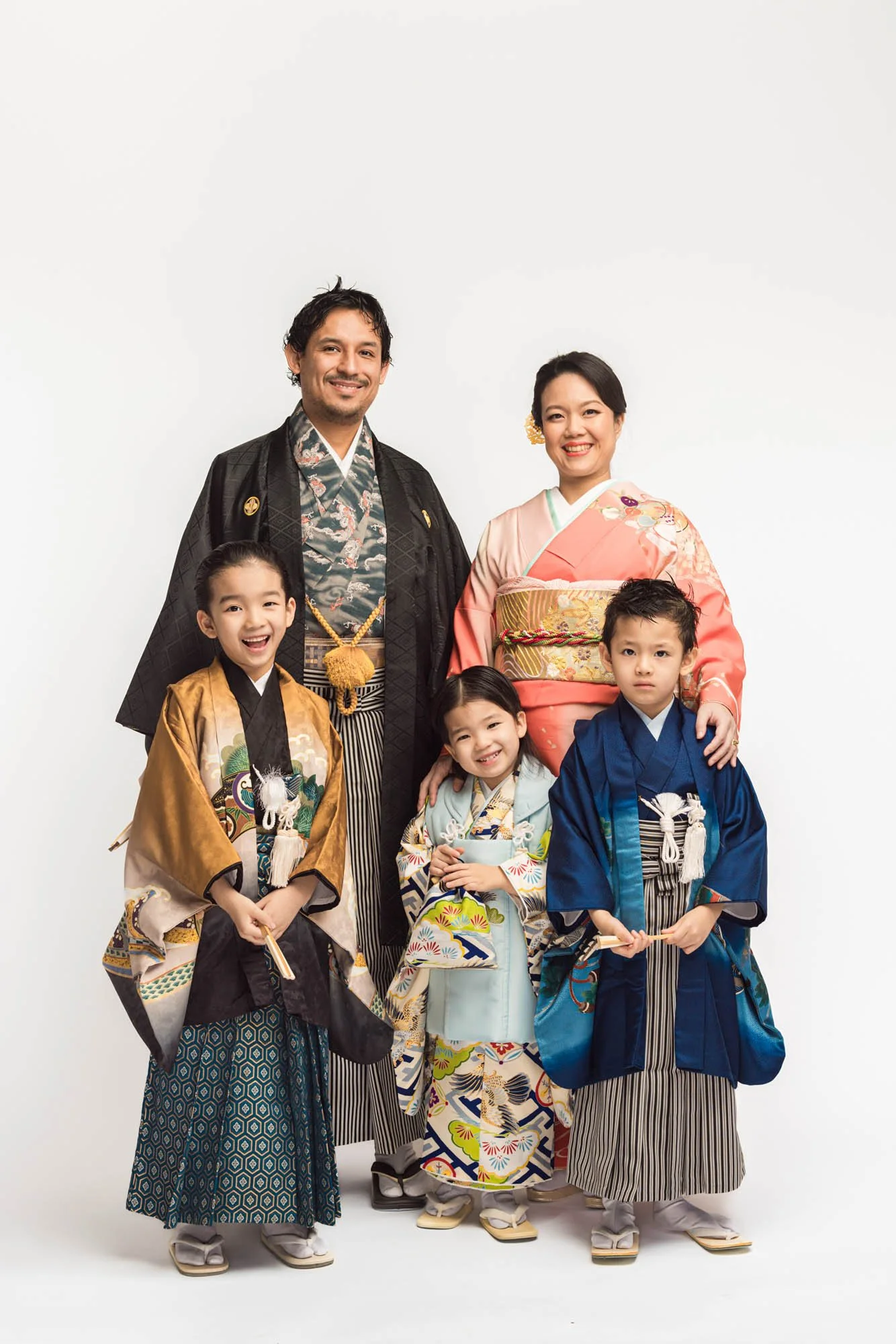 Family portrait of parents and three children wearing traditional Japanese kimono, smiling together in a studio setting in Kirkland, Washington, celebrating Shichigosan with elegant, colorful attire.